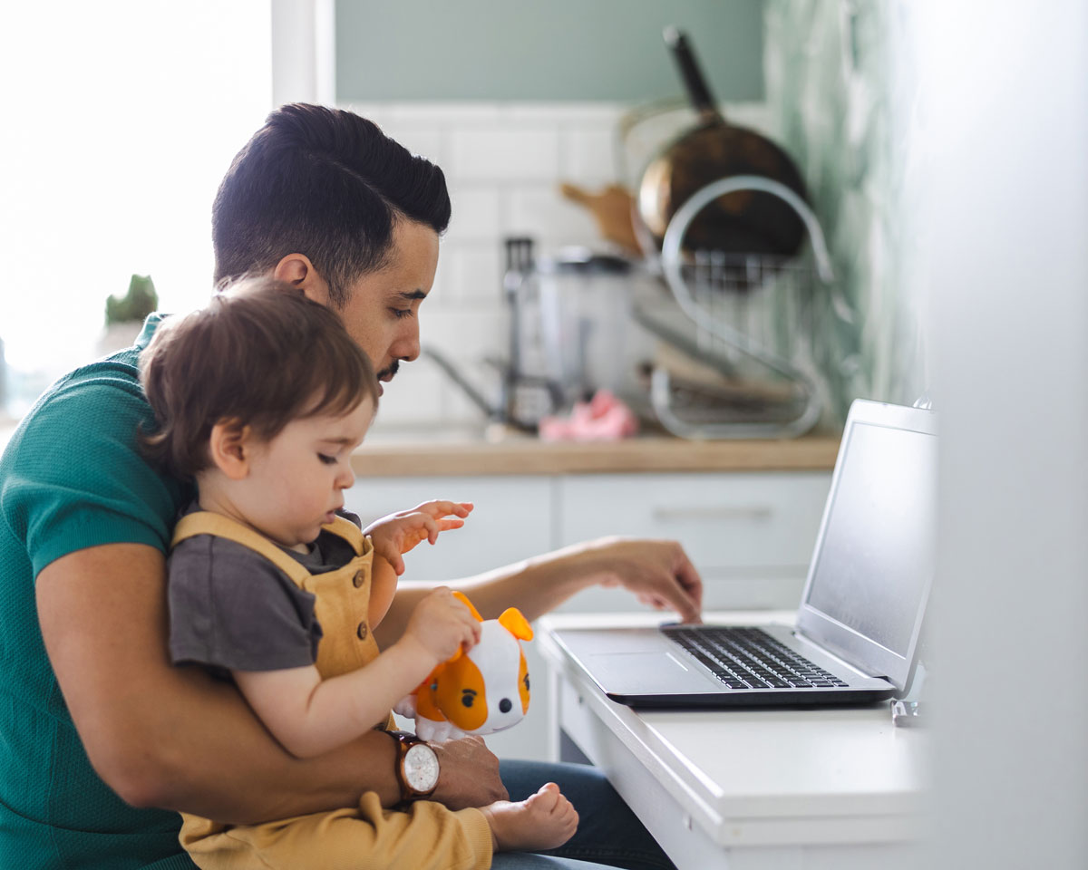 A person sitting at a laptop with a young child on their lap.